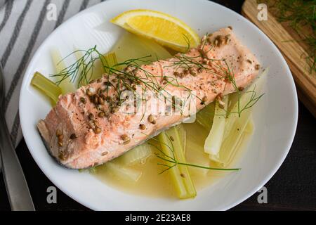Salmone in camicia con finocchio e limone: Un pezzo di salmone erbaciato su finocchio bollito cotto in brodo di limone Foto Stock