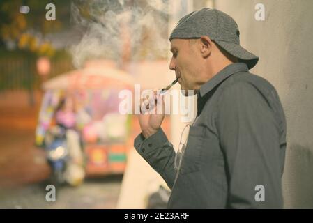 Uomo maturo di fumare sigarette elettroniche per le strade di notte Foto Stock