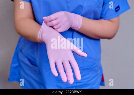 Il medico mette su guanti protettivi rosa, primo piano. Mani di un medico in una divisa blu. Foto Stock