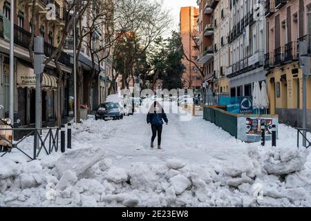 Una donna che indossa una maschera facciale cerca di attraversare una strada coperta di neve.dopo una pesante nevicata in Spagna, Madrid, la capitale spagnola, è immersa nel caos a causa del ghiaccio causato dalle basse temperature. La tempesta di neve Filomena lascia il posto ad un anticiclone che causerà temperature minime fino a -15ºC, e gelate di rischio serio. Secondo l'Agenzia Meteorologica di Stato (AEMET per il suo acronimo in spagnolo) queste sono temperature storiche a Madrid. Foto Stock