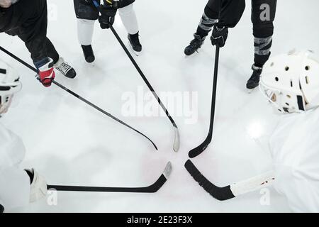 Gruppo di giocatori di hockey in uniforme sportiva, guanti e pattini che si trovano in cerchio sulla pista di pattinaggio e tengono i loro bastoni di fronte a se stessi Foto Stock