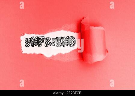Unfriend è una nuova parola in inglese, scritta su un documento rosso strappato. Foto Stock