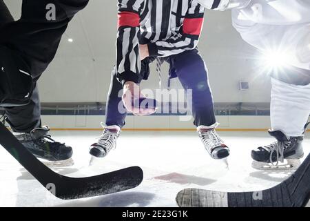 Arbitro di Hockey con puck in piedi su pista di ghiaccio tra due giocatori con bastoni in attesa di essere il primo momento per scattare durante l'allenamento Foto Stock