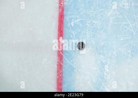 Puck nero sdraiato dalla linea rossa sulla pista di ghiaccio per giocare a hockey su uno stadio che può essere utilizzato come sfondo per annunci o annunci sportivi Foto Stock