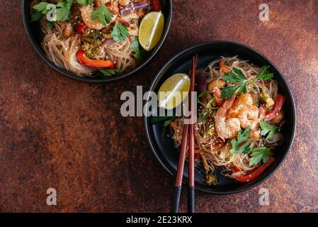 Mescolare gli spaghetti fritti con gamberi e verdure in un wok su un tavolo scuro, vista dall'alto Foto Stock