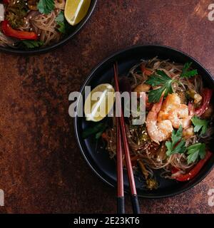 Mescolare gli spaghetti fritti con gamberi e verdure in un wok su un tavolo scuro, vista dall'alto Foto Stock