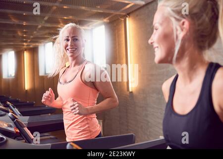 Le amiche sorridono e si guardano mentre si allenano su tapis roulant Foto Stock