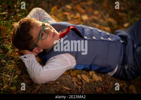 Ragazzo in occhiali e un vestito con una cravatta rossa sdraiato appoggiandosi sulle mani Foto Stock