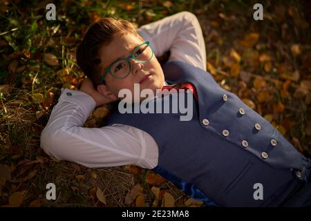 Ragazzo in occhiali e un vestito con una cravatta rossa sdraiato appoggiandosi sulle mani Foto Stock