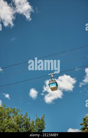 Da sotto gondola blu che si muove sulla strada a rondolo contro il cielo blu nuvoloso sopra gli alberi nel parco a Madrid, Spagna Foto Stock