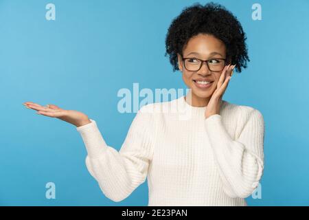 Donna africana sorridente con capelli ricci che tengono spazio copia sul palmo per la pubblicità, l'offerta, il prodotto Foto Stock