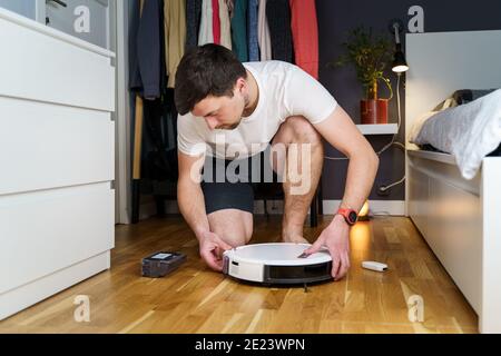 Concetto di casalinghi e tecnologia. Manutenzione ed assistenza di aspirapolvere robot. Pulizia, riparazione, sostituzione delle parti. Uomo che ripara il pulitore robot Foto Stock