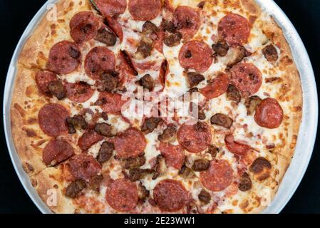 Vista panoramica di pepperoni e salsiccia dominano la parte superiore della pizza di carne al formaggio fuso. Foto Stock