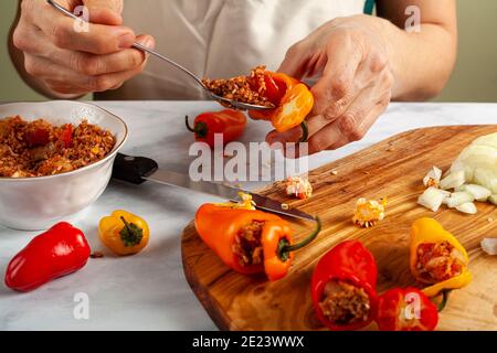 Una chef donna sta riimbottendo i peperoni usando un cucchiaio di metallo. Ha riso ripieno di cipolle, carne macinata, pomodoro, erbe, spezie. Si tratta di un Turco tradizionale Foto Stock