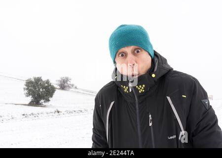 Uomo sorridente con cappotto e cappello, nel mezzo di una nevicata. Spagna. Foto Stock