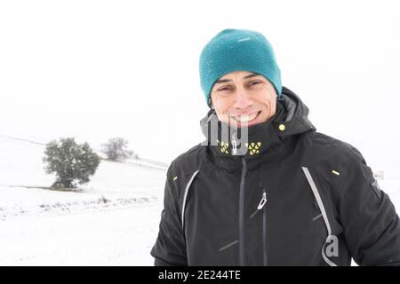 Uomo sorridente con cappotto e cappello, nel mezzo di una nevicata. Spagna. Foto Stock