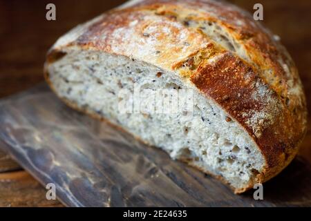 Una pagnotta rotonda di pane fatto in casa a grani interi senza lievito si trova su una tavola di legno. Pasticceria fresca per una dieta sana. Foto Stock