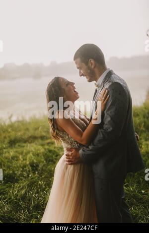 Immagine emozionale di coppia appena sposata in piedi in campo e baciando. Fiume in background.Couple gol. Foto Stock