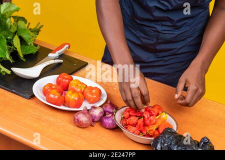chef africano che prepara un piatto, solo a mani, con ingredienti come peperoni, pomodori, cipolle e verdure sul tavolo Foto Stock