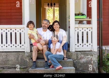 Genitori con due figlie seduti davanti a casa Foto Stock