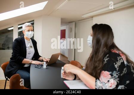 Donne colleghi con maschere facciali protettive che parlano in ufficio Foto Stock