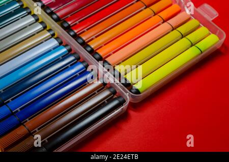 Ampio set di penne colorate con punta in feltro per disegnare su uno sfondo colorato. Scatola in plastica con pennarelli di diversi colori e sfumature. Messa a fuoco selettiva. Foto Stock