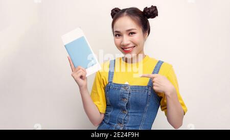 Giovane bella donna turistica asiatica in vacanza tenendo passaporto puntando con le dita, simbolo eccellente Foto Stock
