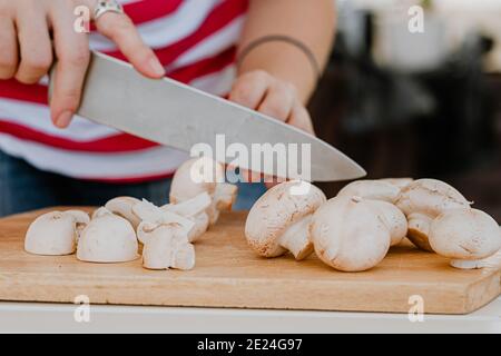 mani che tagliano i funghi con un coltello su una tavola di legno Foto Stock