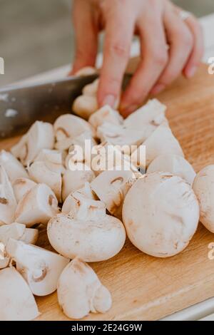 mani che tagliano i funghi con un coltello su una tavola di legno Foto Stock