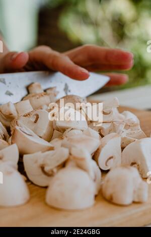 mani che tagliano i funghi con un coltello su una tavola di legno Foto Stock