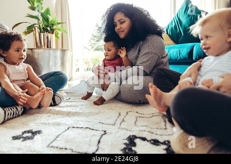 Madri e loro figli insieme. Donne con i loro bambini seduti a terra a casa. Foto Stock