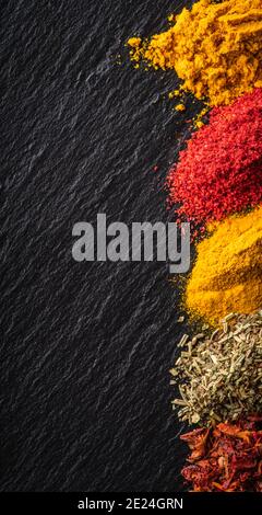 Spezie luminose e colorate sullo sfondo di pietra nera. Spezie ed erbe diverse per lo sfondo. Foto Stock