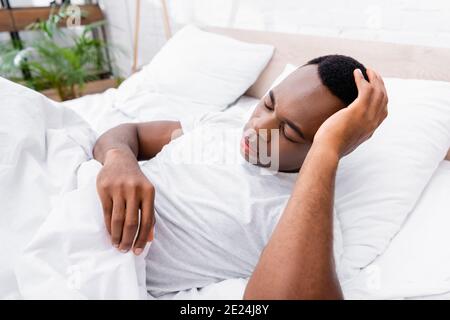 Uomo afro-americano che tocca la testa mentre si sdraiò a letto Foto Stock