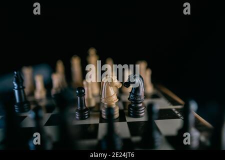 Due pedine di cavalli che si affacciano l'una sull'altra su una scacchiera in uno stile scuro. Concetto di amore interrazziale. Messa a fuoco selettiva Foto Stock