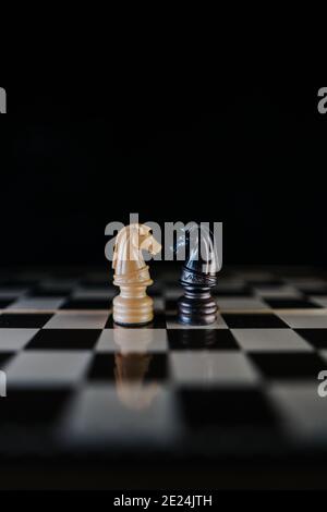 Due pedine di cavalli che si affacciano l'una sull'altra su una scacchiera in uno stile scuro. Concetto di amore interrazziale. Verticale Foto Stock