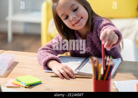 Sorridente ragazza che prende la matita colorata dal titolare alla scrivania con appunti e note adesive su un primo piano sfocato Foto Stock