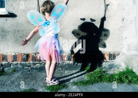 Ragazza che indossa un costume da fata che crea ombre su una parete Foto Stock