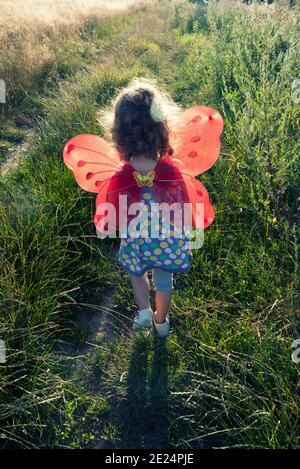 Ragazza che indossa le ali di fata che cammina in un paesaggio rurale, Italia Foto Stock