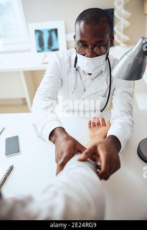 Medico afroamericano fissando un bracciale per la pressione sanguigna su una mano Foto Stock