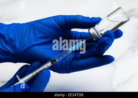 Mani in guanti chirurgici preparazione di siringa medica e ago per iniezione ipodermica su un piano di marmo. Foto Stock