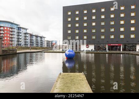 Walsall, West Midlands, Regno Unito. 12 gennaio 2021. Gli installatori di una boa di avvertimento di 6 piedi di diametro nel canale del bacino di Walsall nelle Midlands occidentali hanno chiesto di mantenere a galla l'allerta di acque profonde per altri cinque anni. Il canale e River Trust sostengono che la sfera blu gonfiata di 2 metri ha salvato molte vite nel corso dei mesi che è stato lì nel canale. Intorno al bacino del canale ci sono bar e ristoranti, così come la Walsall New Art Gallery, e i visitatori e i pub spesso confondono le alghe che crescono in estate per l'erba - con il risultato di alcune sorprese bagnate. Peter Lopeman/Alamy Live nuovo Foto Stock