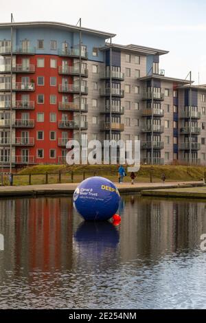 Walsall, West Midlands, Regno Unito. 12 gennaio 2021. Gli installatori di una boa di avvertimento di 6 piedi di diametro nel canale del bacino di Walsall nelle Midlands occidentali hanno chiesto di mantenere a galla l'allerta di acque profonde per altri cinque anni. Il canale e River Trust sostengono che la sfera blu gonfiata di 2 metri ha salvato molte vite nel corso dei mesi che è stato lì nel canale. Intorno al bacino del canale ci sono bar e ristoranti, così come la Walsall New Art Gallery, e i visitatori e i pub spesso confondono le alghe che crescono in estate per l'erba - con il risultato di alcune sorprese bagnate. Peter Lopeman/Alamy Live nuovo Foto Stock