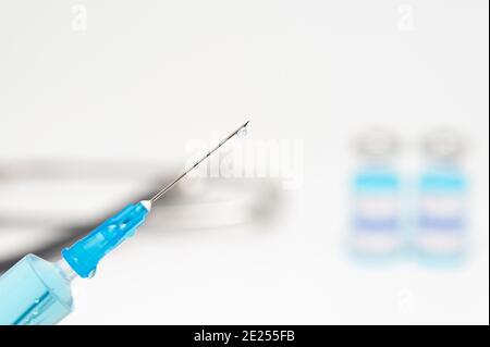 Concetto medico - primo piano della siringa con ago contenente liquido blu. Sfondo offuscato con fiale per vaccino e stetoscopio. Spazio di copia. Foto Stock