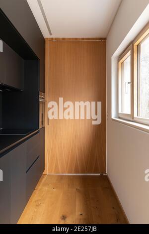 Interni moderni con pareti bianche e pavimenti in parquet. Elegante cucina nera con grande porta chiusa in legno. Nessuno dentro Foto Stock