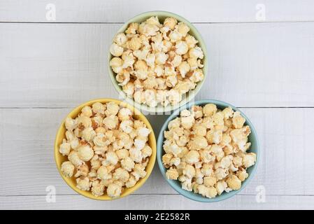 Colpo di testa di tre diverse ciotole colorate riempite di popcorn fresco, su un tavolo di legno bianco. Foto Stock