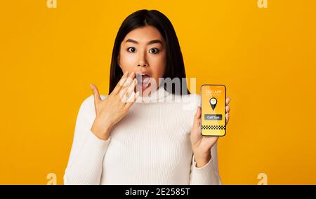 Sorprendo Asian Lady Holding smartphone con app aperta per Taxi Ordine Foto Stock