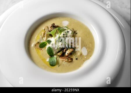 Crema di carciofi con funghi e mousse di formaggio, con germogli verdi in piatto bianco, vista dall'alto Foto Stock