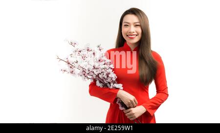 Donna asiatica in rosso tradizionale vietnamita vestito in piedi, mano tenere pesca fiore ramo, sentire felice e speranza. Foto Stock