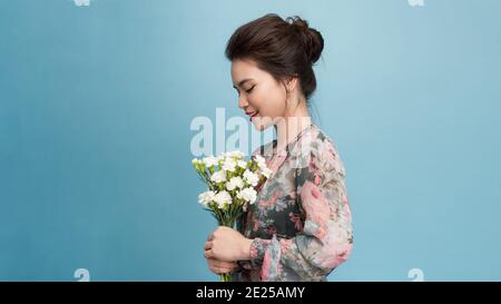 Ritratto di donna piacevole osservante ha make up minimo, ampio sorriso, riceve fiori in occasione speciale, isolato su sfondo azzurro chiaro Foto Stock