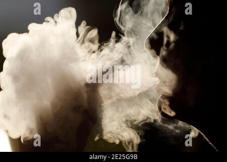 Profilo silhouette di una donna che fuma. Fumo bianco intenso. Sigaretta elettronica. Francia. Foto Stock